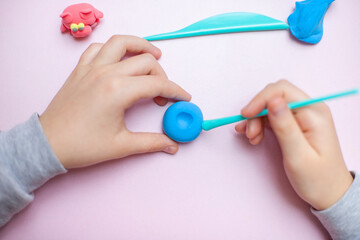 Hands of a child playing with colored air dry clay  on a pink background