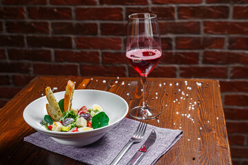 Salad with prosciutto, slices of grapes and cherry tomatoes, quail eggs on a plate and a glass of wine, dark and moody, top new