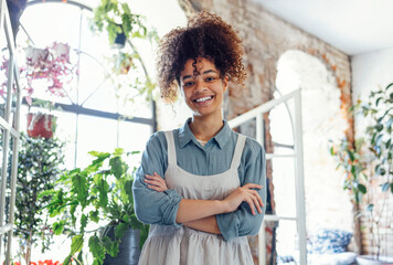 Young black woman wearing beige apron on flower shop background with copy space