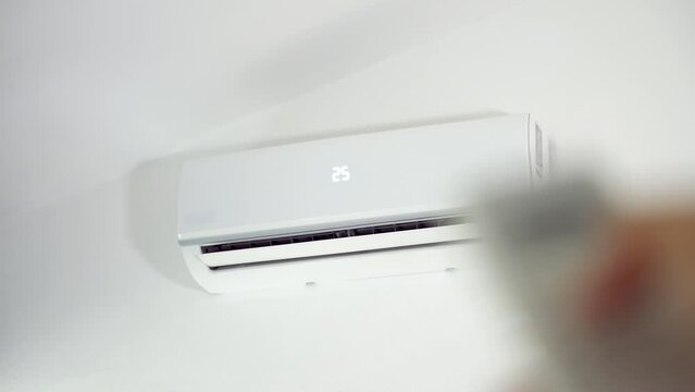 Close up of man turns on the white air conditioner at 25 degrees on the wall with the remote control inside the living room. Comfortable temperature in the bedroom during hot weather