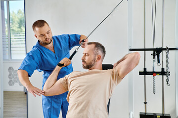 experienced physiotherapist helping man with recovery training on exercise machine in kinesio center