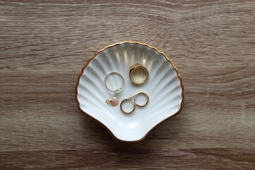 Ring dish shaped like a seashell with gold rings, earrings and pendant. Wooden background, top view.