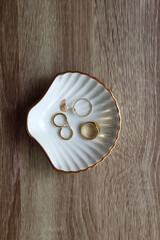 Ring dish shaped like a seashell with gold rings, earrings and pendant. Wooden background, top view.
