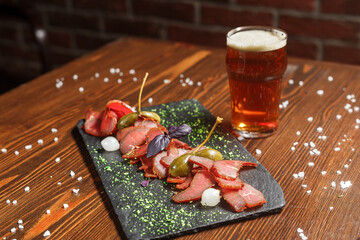 dried meat delicacy, basturma cut into pieces with cappers, on a slate board, beer glass, dark and...