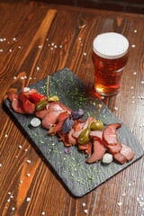 dried meat delicacy, basturma cut into pieces with cappers, on a slate board, beer glass, dark and moody, top new