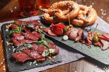 a set of deli meats for beer, dry-cured meat cut into pieces with cappers, on a slate board, beer...