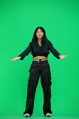 A woman in black clothes, on a green background, in full height, spreads her arms