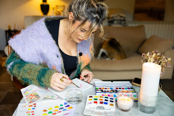 Photo of young woman painting in watercolors comfortably at home