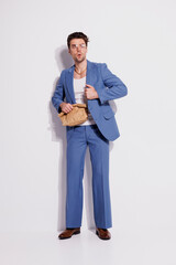 Scared and stylish man in suit holding paper bag on grey with shadow