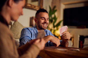 A smiling man playing cards with her female partner, staying at home, enjoying the fun night. - obrazy, fototapety, plakaty