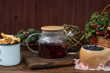A bouquet of ripe red lingonberry berries in a wicker basket and a kettle of lingonberry tea. Forest orange chanterelle mushrooms