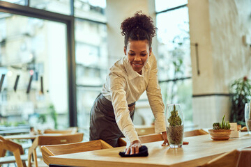 An African waitress working at the cafe, using a cloth and cleaning the table.