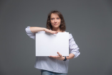 A young woman smiles and holds a white sheet in front of her on a gray background.