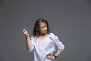 A young woman thoughtfully snaps the fingers of her right hand on a gray background.