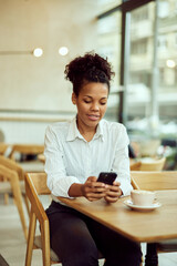 A smiling African woman sitting alone at the cafe, using a mobile phone.