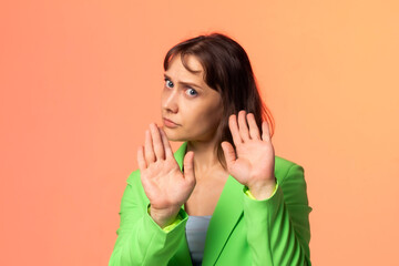 A woman in a light green suit on an orange background holds her hands in front of her, moving away...