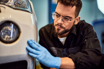 A male mechanic wearing gloves is looking at the scratch on the car.