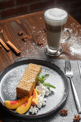 Honey cake with peaches on a black plate, glass with cappuccino, dark and moody, top new