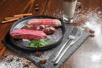 several eclairs lie on a black plate and a glass of cappuccino, dark and moody, top new