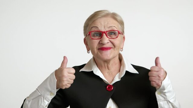 Pretty blonde old lady enjoying success, victory. Smiling elegant elderly woman with bright make-up in red-rimmed spectacles in white shirt, black jacket. High quality 4k footage