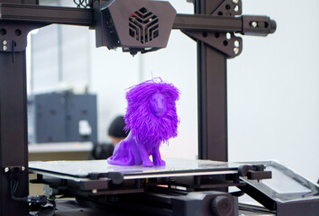 Model of toy lion printed on 3D printer from melted plastic purple color on desktop of 3D printer....