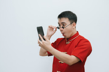 Shocked face of Asian man wearing Cheongsam and black vintage sunglasses while looking at the...