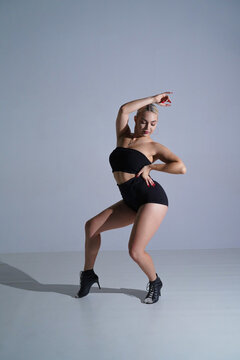 Female dancer in black shorts and top dancing in high heels. Young woman posing and showing body flexibility in studio on white background.