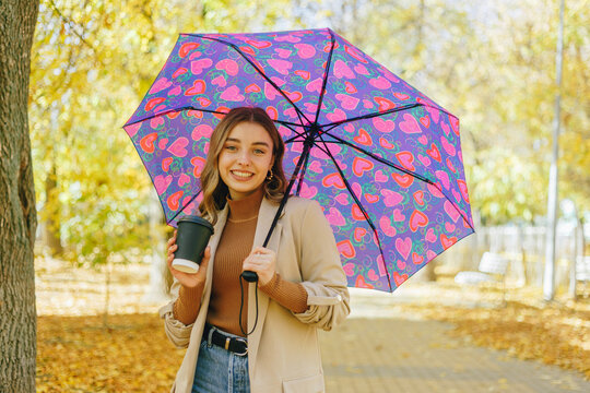 Happy young woman with umbrella walking in autumnal park
