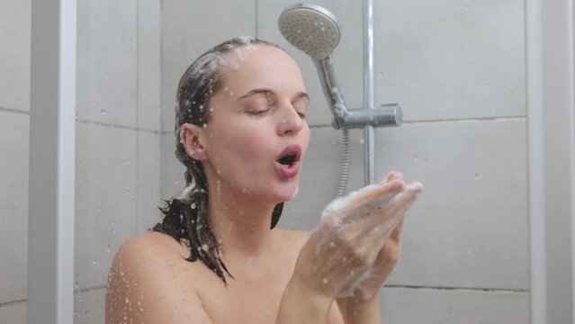 Caucasian young naked woman washing her hair in shower with shampoo foam cleanses her body creating refreshing and revitalizing routine reveling in natural freshness of water