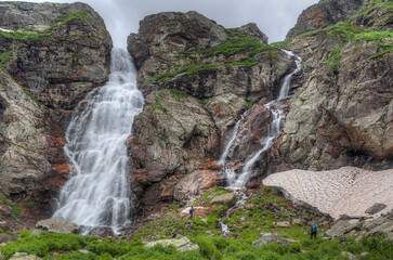 Waterfall in a mountain valley. small figures of people against the backdrop of mountains.