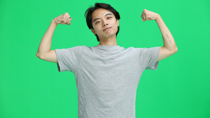 A guy in a gray T-shirt, on a green background, close-up, shows strength