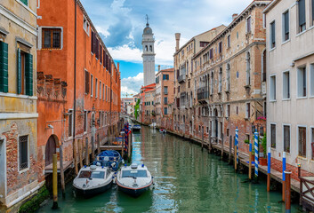 Narrow canal with boats and leaning bell tower in Venice, Italy. Architecture and landmark of...