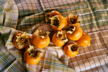 Ripe persimmon lies on a bent checkered tablecloth on the table. Top view