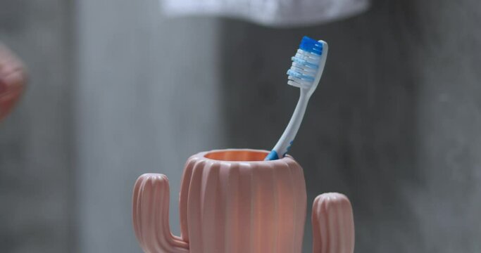 Male hand putting toothbrush in cup. Removal of plaque accumulated overnight. Morning routine procedure, brushing teeth with special orthodontic brush. Man's hand picks up brush and puts back in cup.