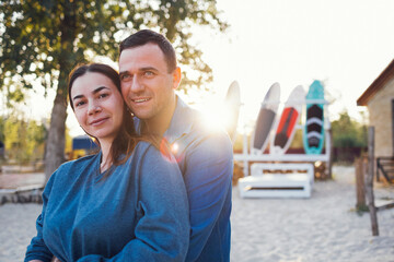 Happy family couple on the beach. Young man hugging beautiful woman on background of surfboards....