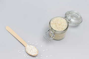 Three types of white rice in glass jar, wooden spoon and bowl.