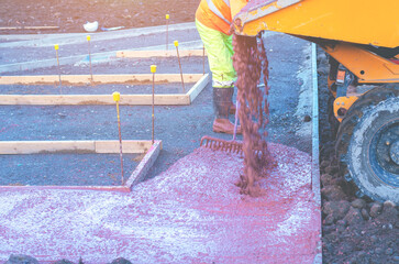 Builders pouring and levelling wet ready-mix concrete into formwork   during new footpath construction - obrazy, fototapety, plakaty