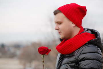 A man in a red hat and scarf is holding a red rose - obrazy, fototapety, plakaty