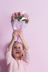A cute little girl in a pink dress holds a bouquet of pink roses