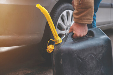 A man filling fuel tank of his car with diesel fuel from the jerry can as there is no fuel at the petrol station, close up - obrazy, fototapety, plakaty