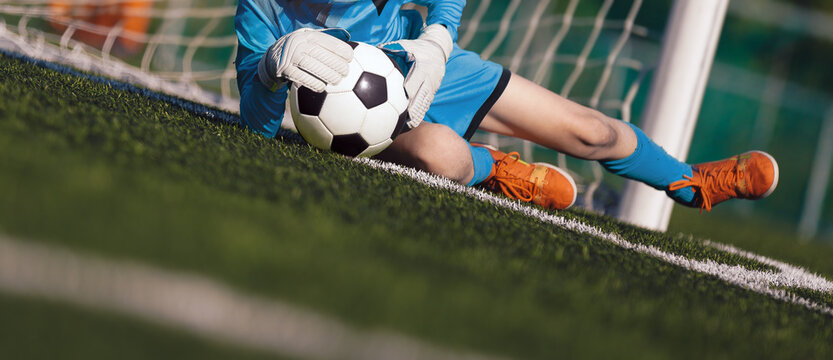 Fototapeta Young boy as a soccer goalie catching the ball during a soccer match. Football goalkeeper in jersey shirt and sports gloves play a football tournament game