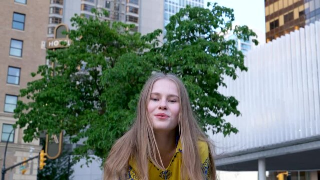 Woman sends air kiss smiling looking at camera. Happy positive emotional blonde girl. Joyful cheerful pretty lady in yellow hoodie, smile face. Indoors studio, isolated. High quality