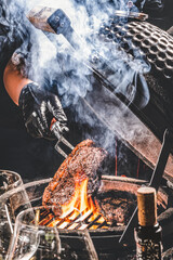 Variety of raw beef meat steaks for grilling with seasoning and utensils on dark rustic board, red tone of fresh food in raw cut