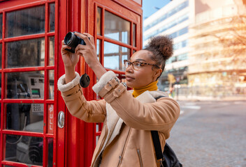 Outdoor portrait of woman using camera   against red phonebox in English city