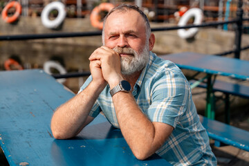 a mature bearded man sitting  on a bench, walking at a quay, enjoying warm days of the spring,...