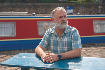 a mature bearded man sitting  on a bench, walking at a quay, enjoying warm days of the spring,...