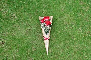 Red rose mix with baby breath in cone shape bouquet lay on the middle of the field