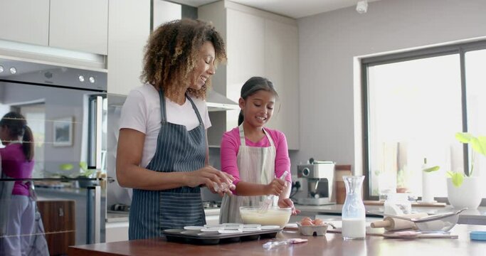 Happy biracial mother and daughter making cake mix, baking in kitchen, copy space, slow motion