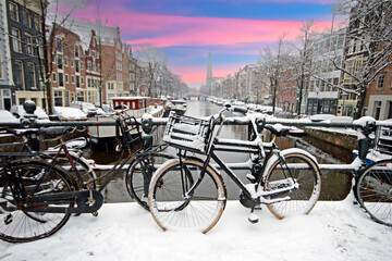 Fototapeta na wymiar Amsterdam covered with snow with the Westerkerk in winter in the Netherlands at sunset