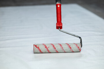 A white paint roller with a red handle. Applying glue to wallpaper - obrazy, fototapety, plakaty